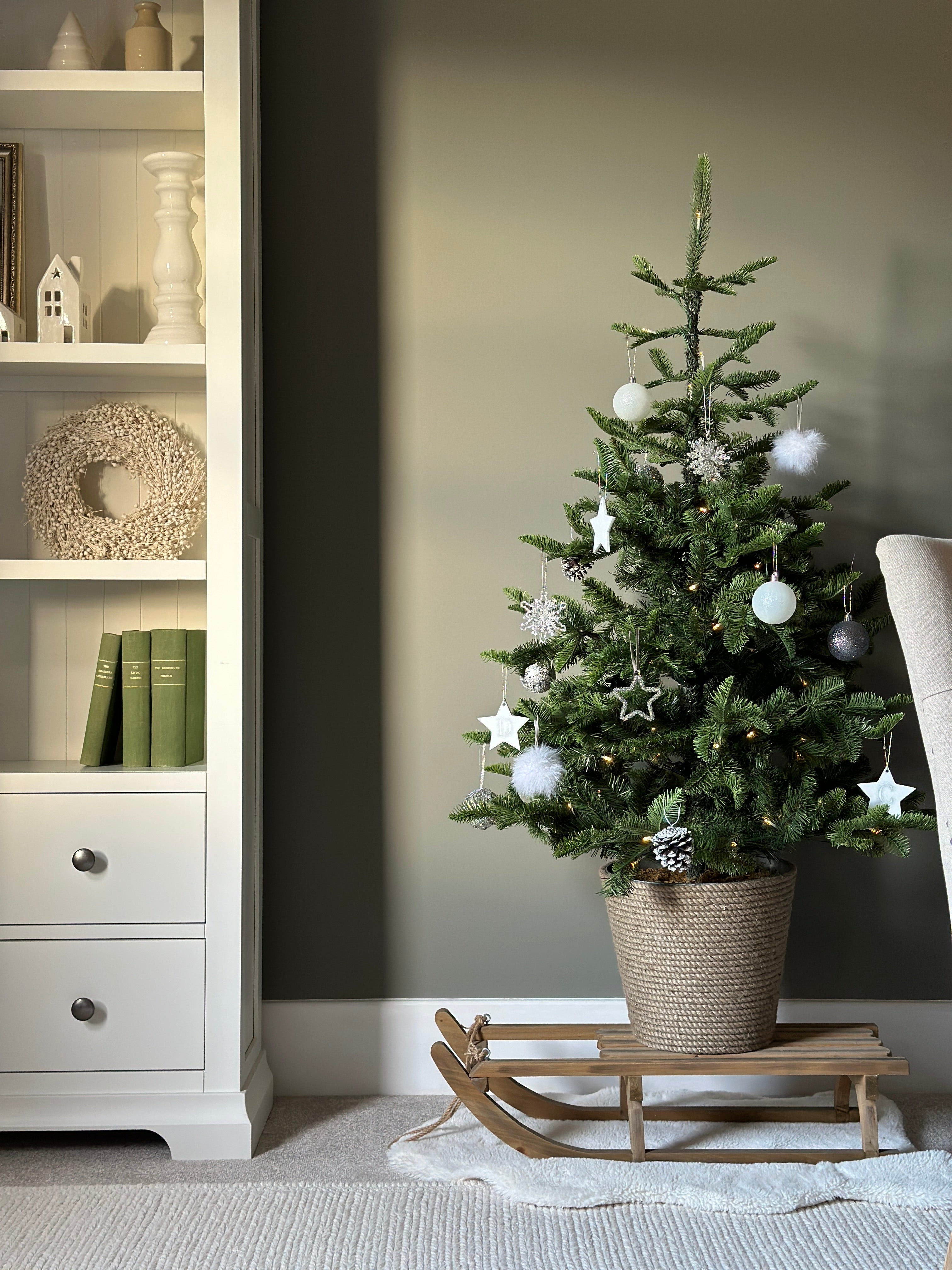 Decorated Christmas tree in a room with a white bookshelf and gray wall.