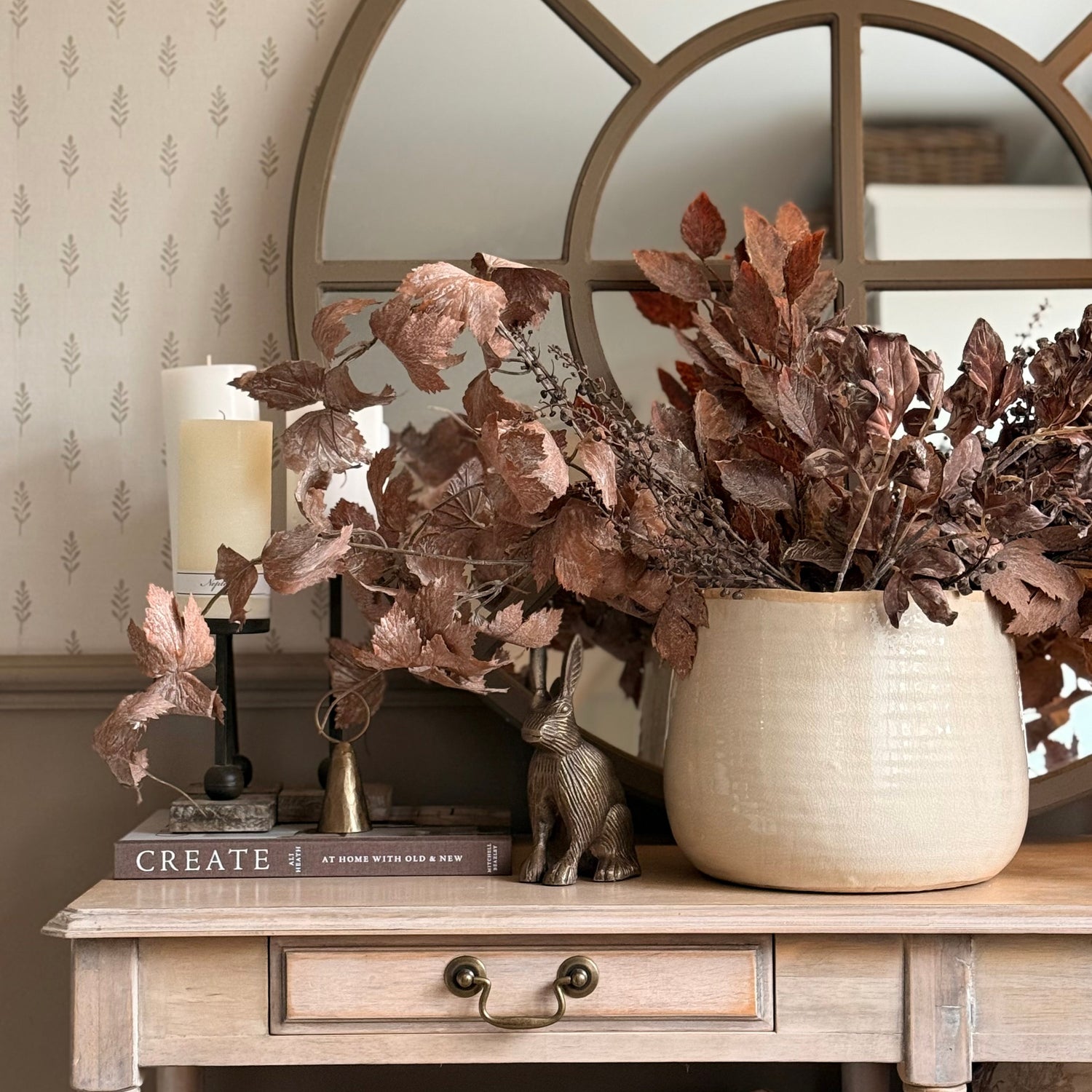 Decorative table with a vase of dried flowers, books, and a candle in a room with patterned wallpaper.